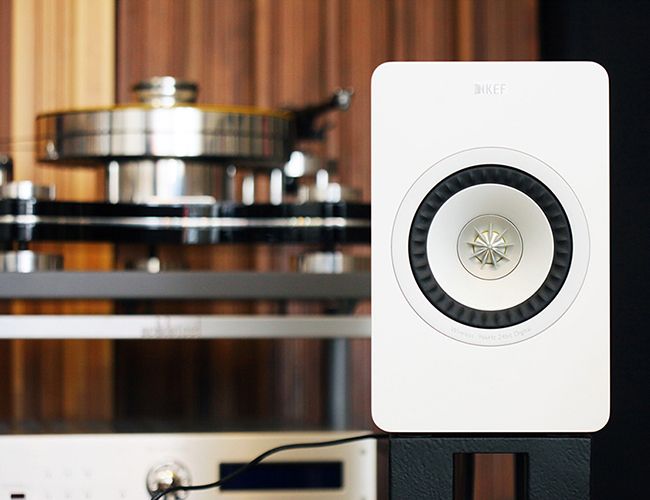 a white speaker sitting on top of a black stand in front of a book shelf