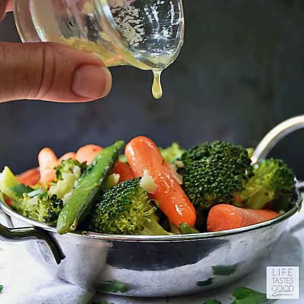 a person pouring dressing onto a bowl full of broccoli, carrots and celery