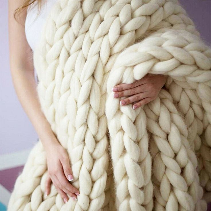 a woman is wrapped up in a giant chunky blanket, with her hands on the back