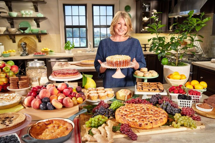 a woman standing in front of a table full of pies and fruit on it