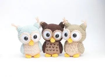 three small crocheted owls sitting next to each other on a white surface with one staring at the camera