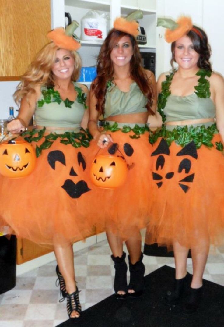 three women dressed up as pumpkins and witches standing in a kitchen with their hands on their hips