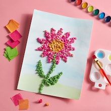 a pink card with a flower on it next to some paint and crayons