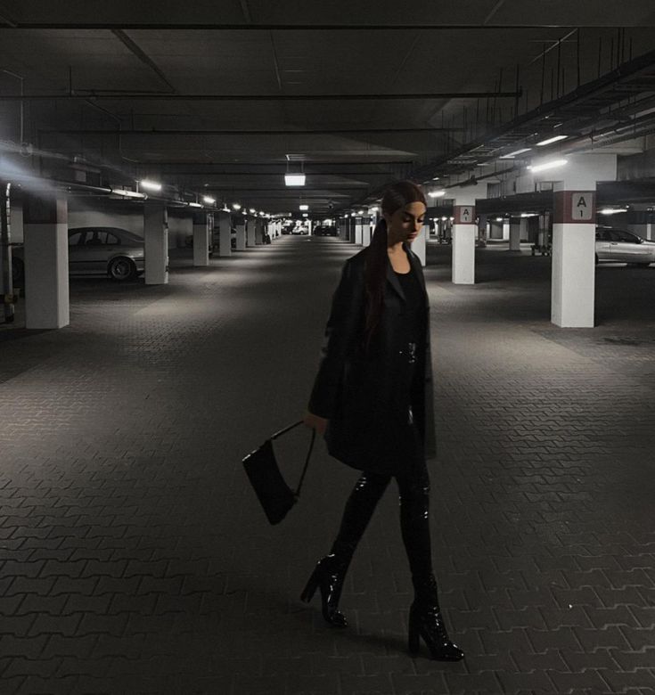 a woman is walking in an empty parking garage with her handbag on her hip