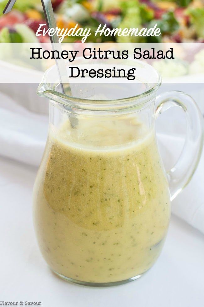 a glass pitcher filled with dressing next to a bowl of salad