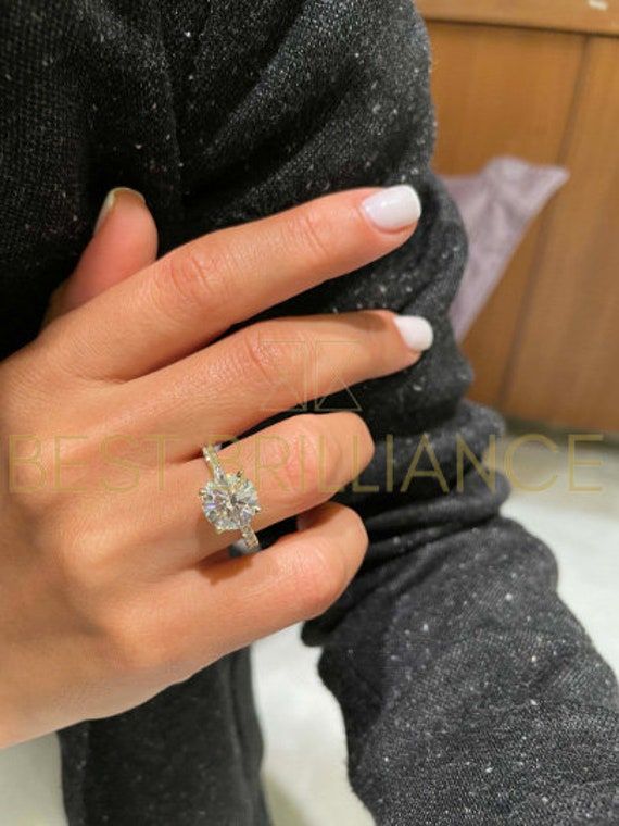 a woman's hand with a diamond ring on her finger and white nail polish