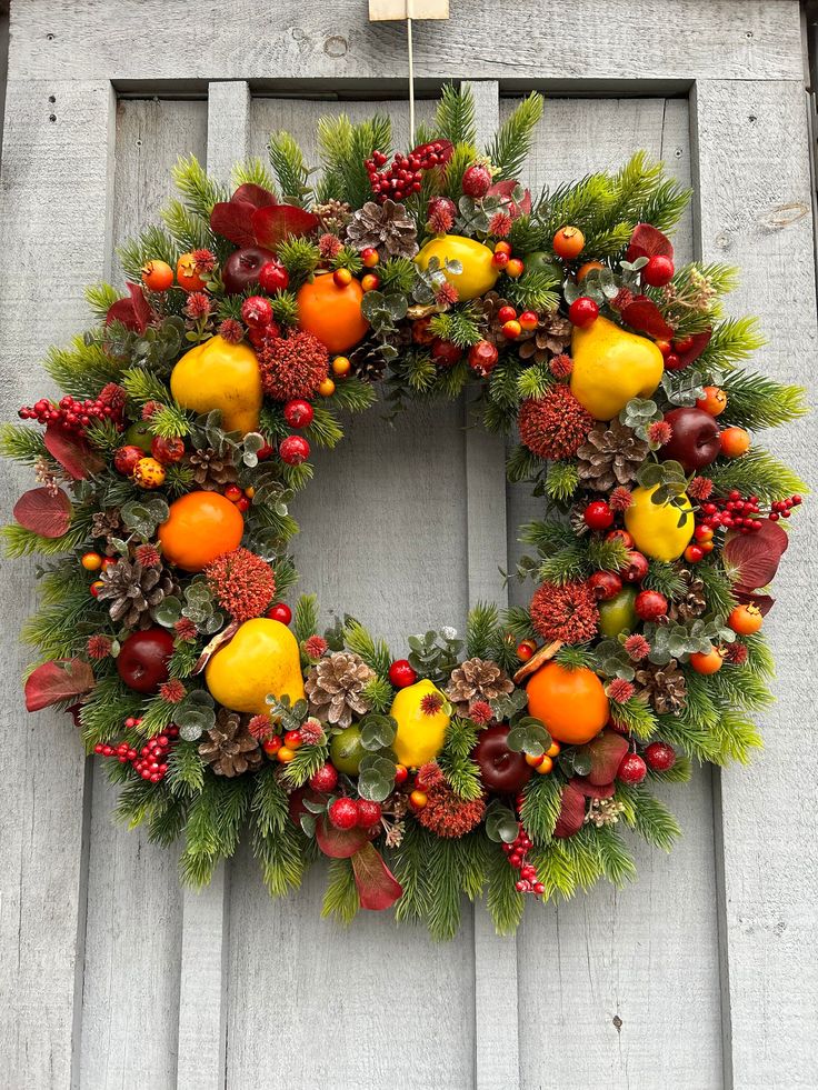 a wreath with fruit and pine cones hanging on the front door to give it a festive feel