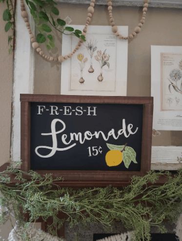 a lemonade sign is hanging on the mantle in front of some framed pictures and other items