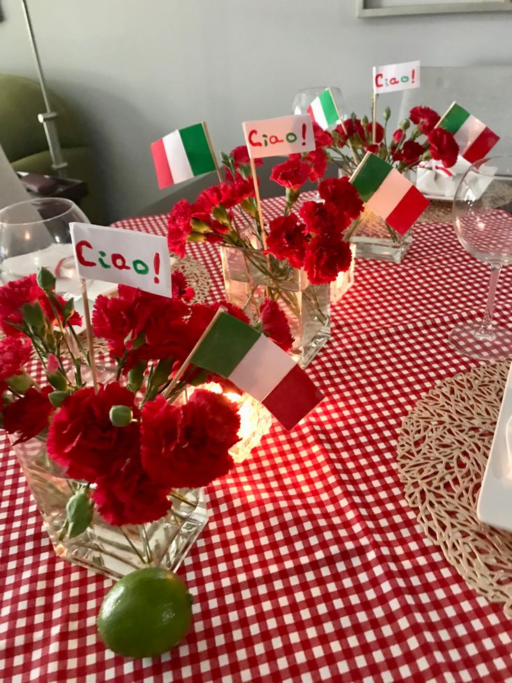 red flowers are in vases on a table with place cards and wineglasses