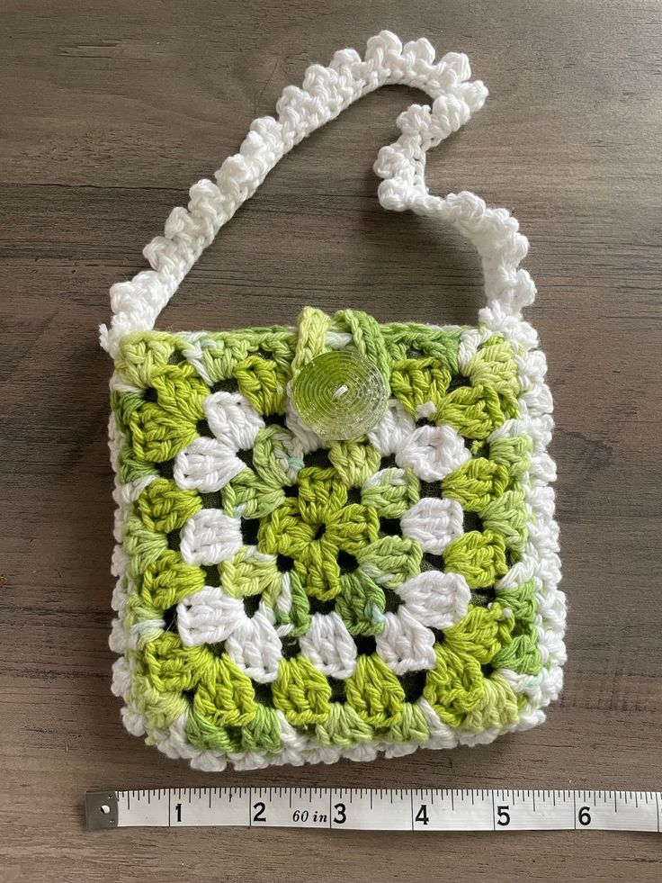 a green and white crocheted purse sitting on top of a wooden table next to a ruler