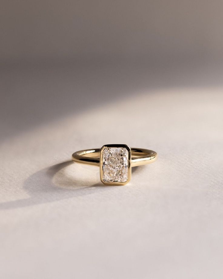 a yellow gold ring with a square diamond in the center, on a white surface