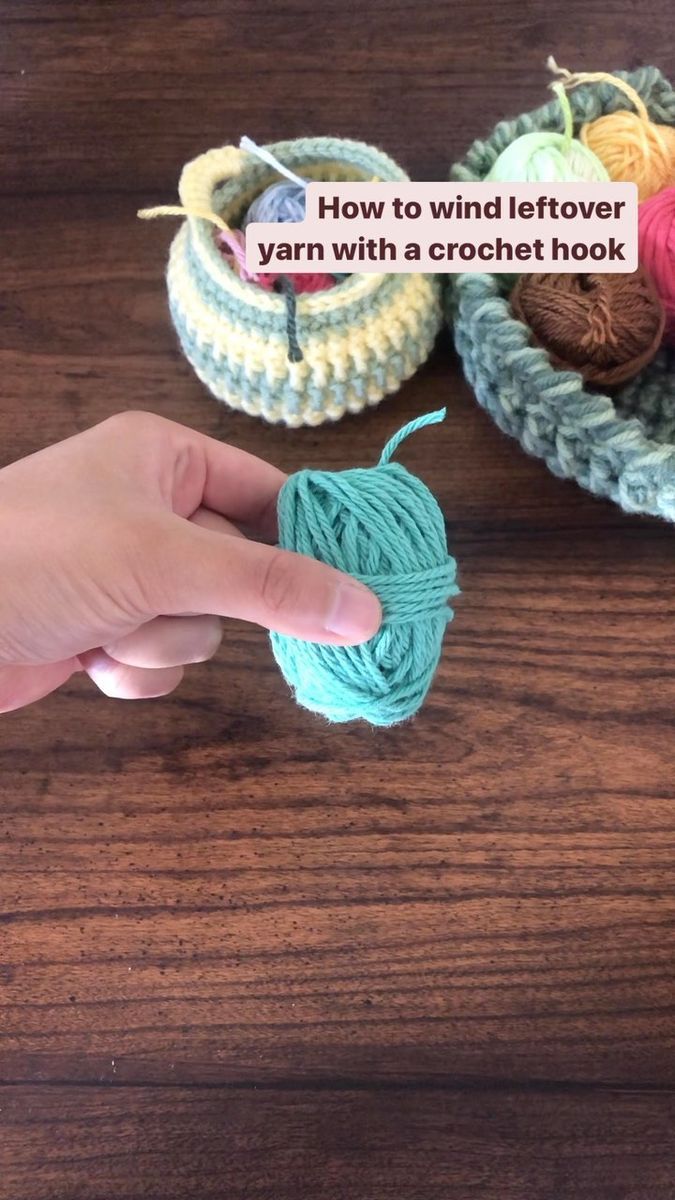 someone is holding yarn in their hand near some crochet hooks on a wooden table