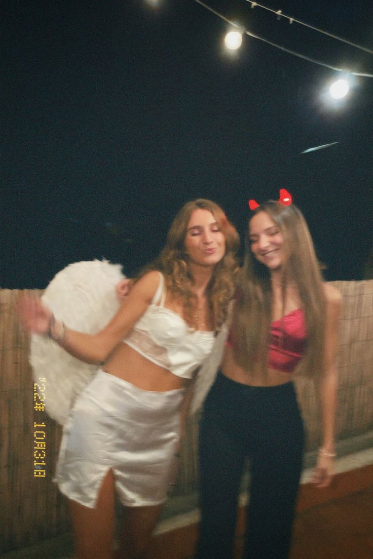 two beautiful young women standing next to each other in front of a fence at night