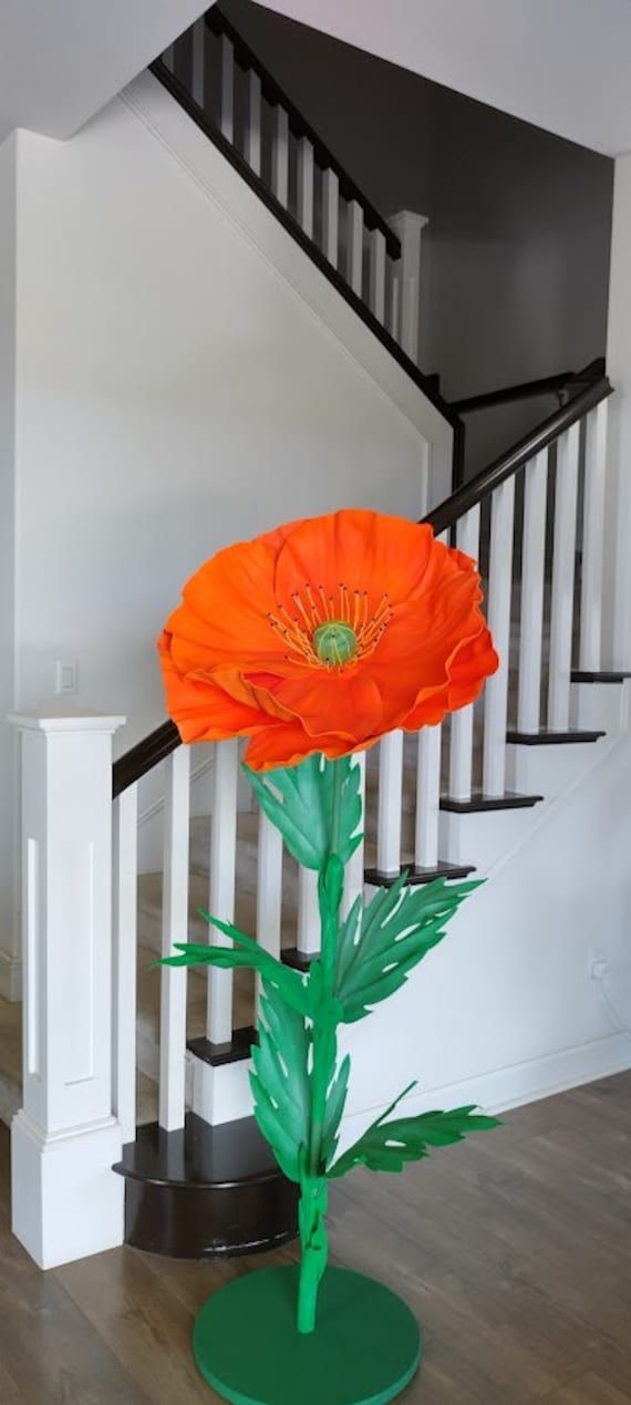 a large orange flower sitting on top of a green plant in front of a stair case