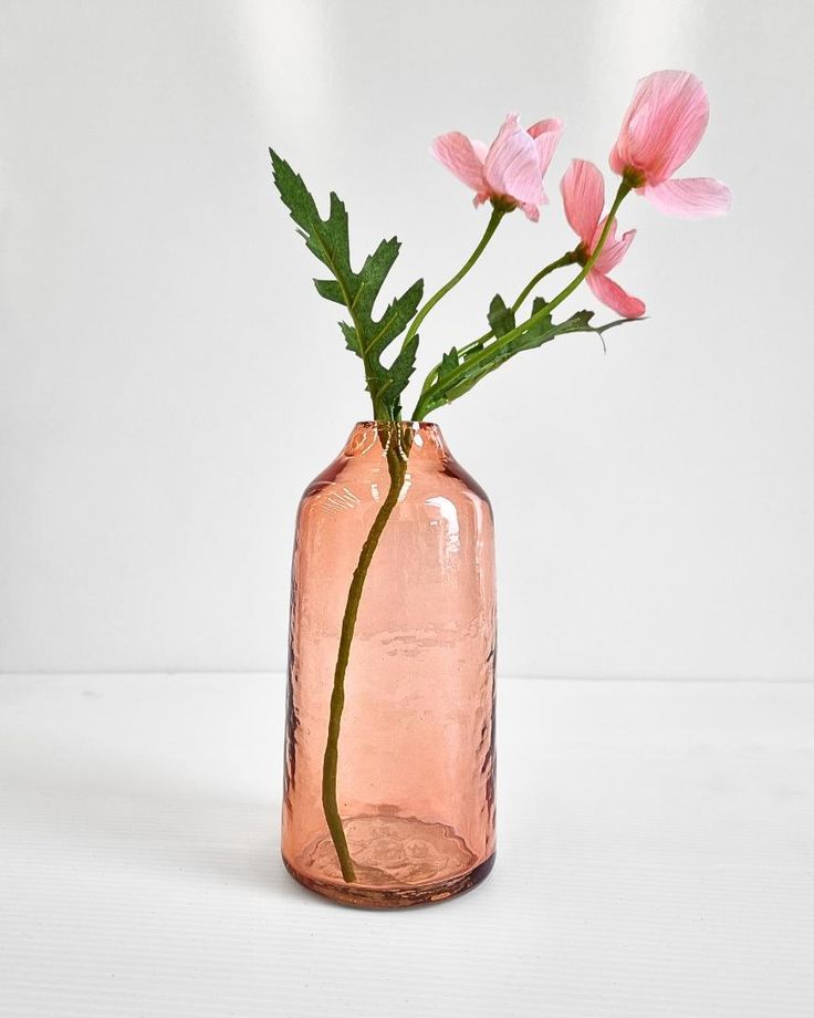 three pink flowers in a glass vase on a white surface