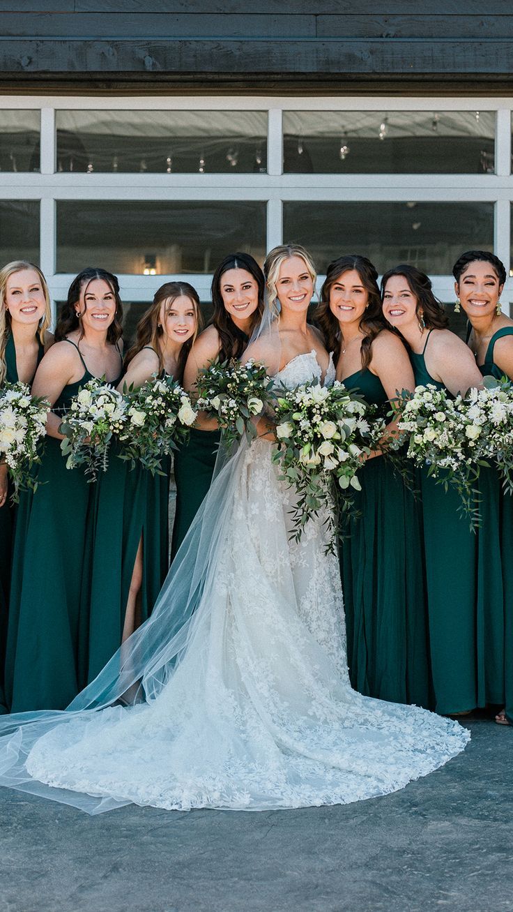 a group of bridesmaids pose in front of a building with their bouquets