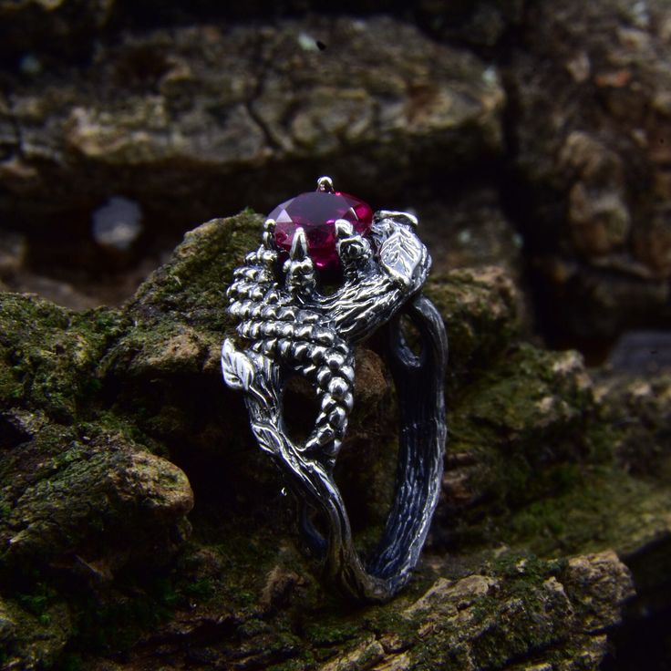 a silver ring with a red stone in the middle on some mossy rocks,