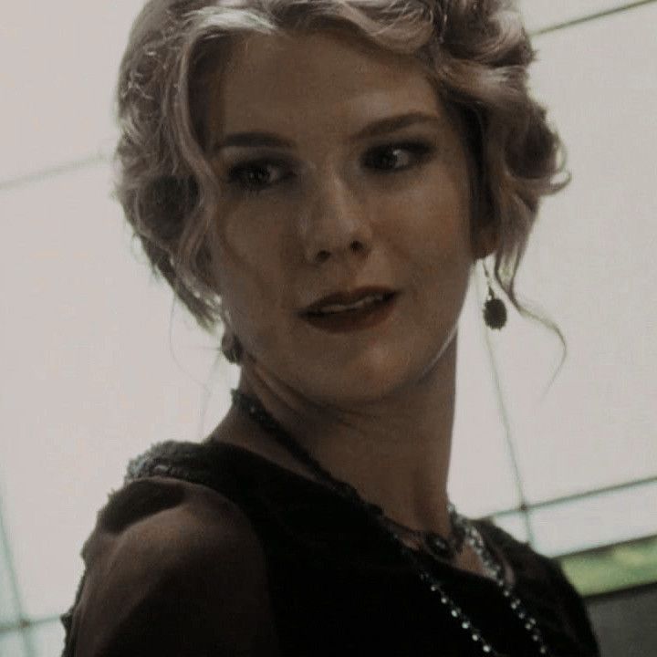 a woman with blonde hair wearing a black dress and pearls on her necklace is looking at the camera