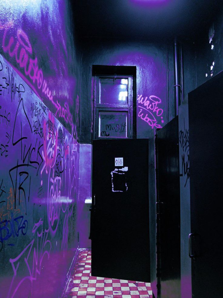 a bathroom with graffiti on the walls and a checkerboard floor in front of two black refrigerators