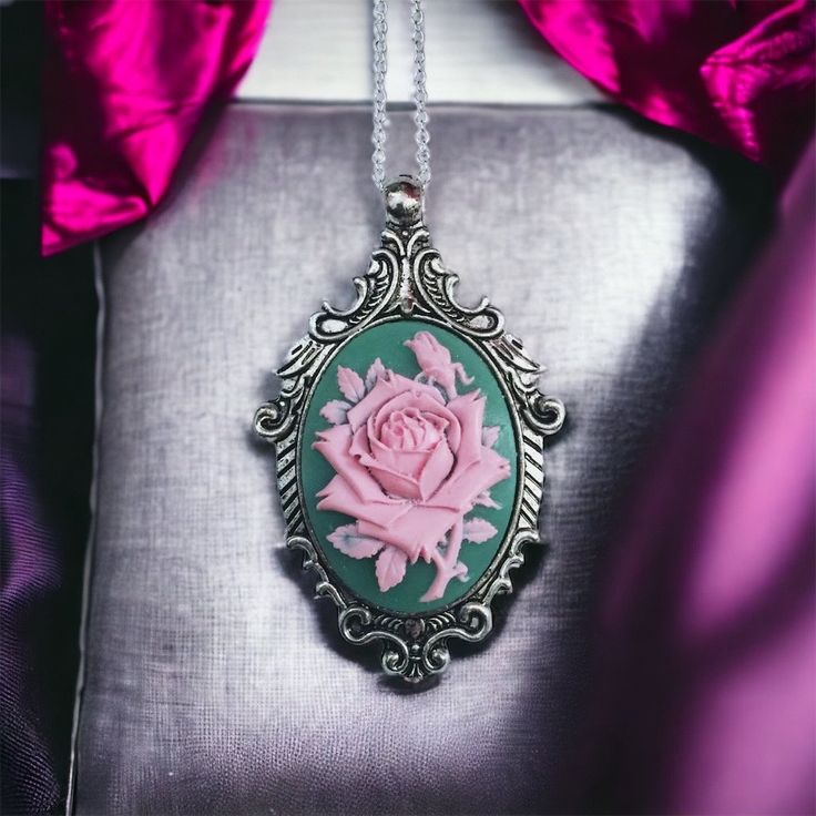 Styled in a majestic fashion with a feminine twist, the Victorian Rose Cameo Necklace is sure to make a statement! Featuring a beautifully detailed cameo with an pink rose on a green resin background.  The Victorian Rose Cameo Necklace is set in a  vintage-style antique silver-plated large pendant. The pendant measures approximately 2.5" long and 2" wide.   Add on a nice antique silver-plated satellite bead chain, that closes with a lobster clasp, and may be added at checkout. Choose your own ne Elegant Rose Red Necklace With Rose Design, Pink Rose Design Pendant Necklace, Elegant Pink Rose Necklace, Pink Rose Pendant Jewelry, Feminine Pink Jewelry With Rose Design, Pink Cameo Jewelry For Formal Occasions, Pink Cameo Necklace For Gifts, Pink Victorian, Floral Pendant