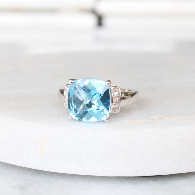 This beautiful statement piece features a square, cushion-cut swiss blue topaz with a bright blue colour. The center stone is set in luxurious 14k white gold, surrounded by three circle-cut diamonds on each shoulder for some added sparkle. The wonderful glow of the blue topaz stands out against the lustrous white gold of the band making this ring a bold, unique engagement ring, anniversary gift, or statement ring. Stones: One genuine cushion-cut swiss blue topaz (approx. 10 mm x 10 mm) Six circle genuine diamonds (approx. 0.06 ctw) Metals: 14k white gold Please allow up to 5 business days for processing. Currently only shipping within Canada and USA. | c u r a t e d | Visit our website for curated and modern pieces  https://www.menkduke.com | f a c e b o o k | Follow us on Facebook for new Ring Stones, Statement Engagement Ring, Topaz And Diamond Ring, Hand Necklace, Jewelry Appraisal, Right Hand Rings, 14k White Gold Ring, Unique Engagement, Blue Colour