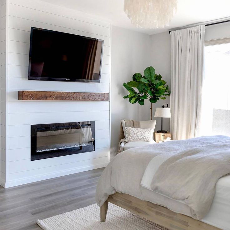 a bedroom with a bed, fireplace and tv mounted on the wall above it's headboard