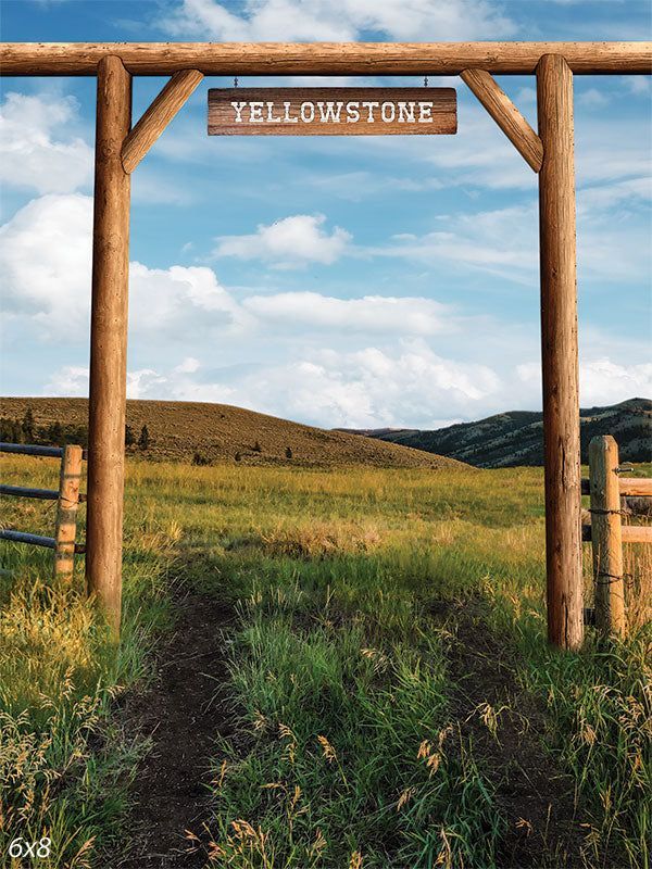 a wooden sign that reads yellowstone in front of a grassy field and fenced in area