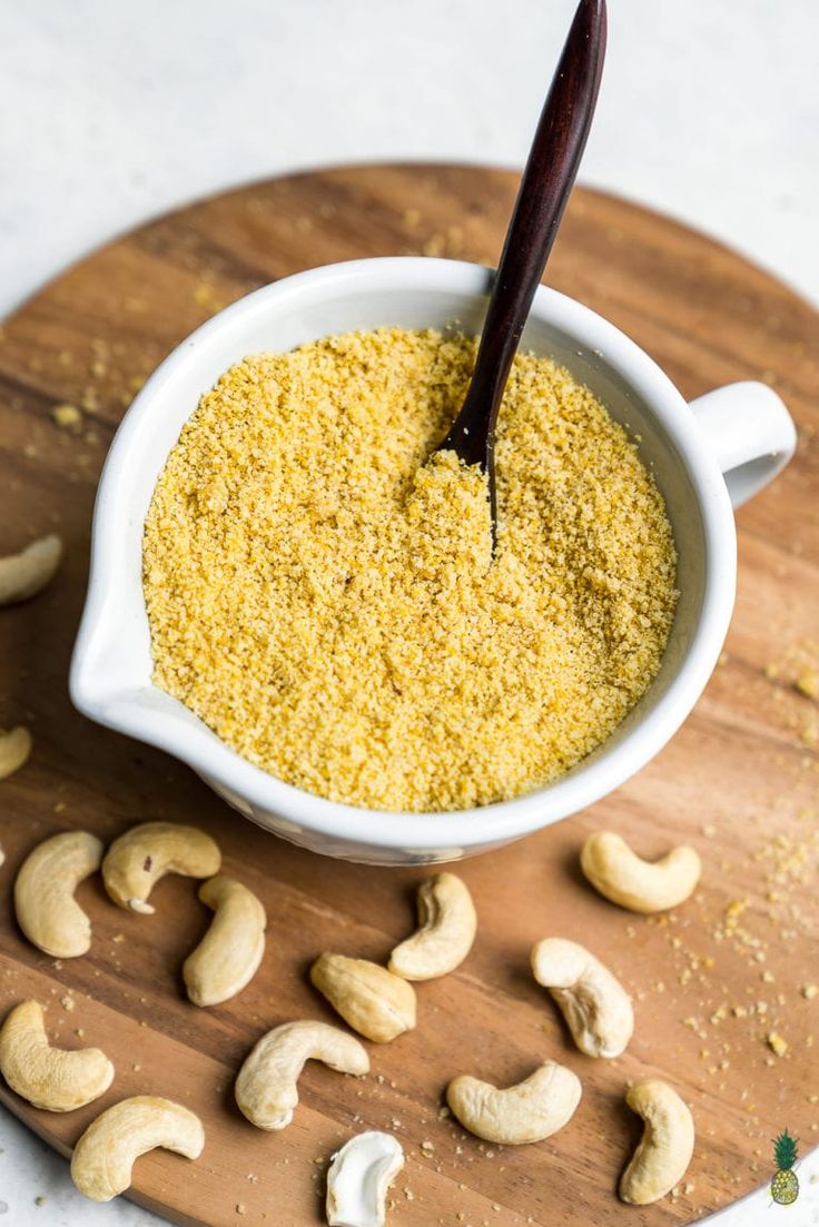 a white bowl filled with cashews on top of a wooden cutting board next to nuts