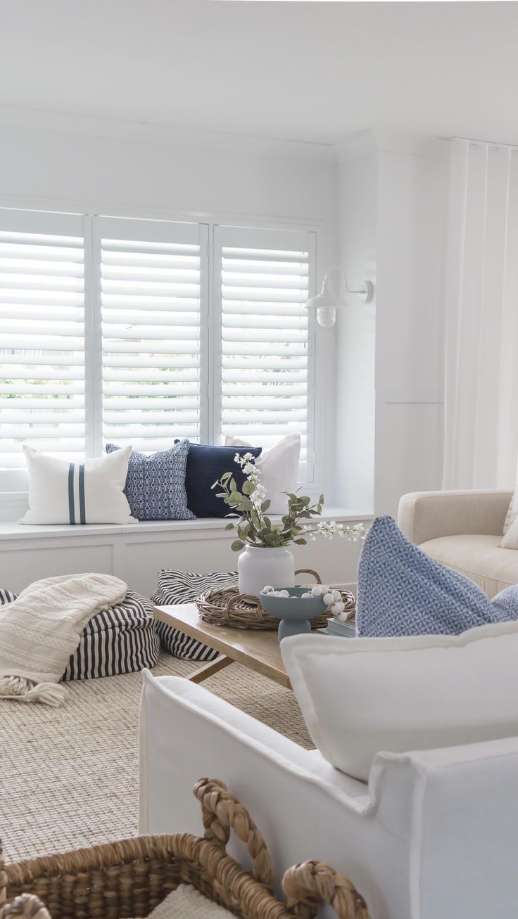 a living room filled with white furniture and lots of windows covered in shuttered shades