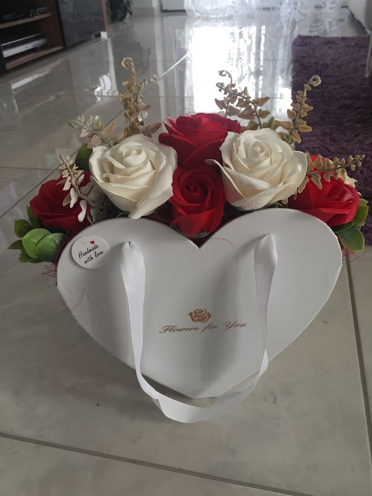 a white heart shaped box with red and white roses in it on a tile floor