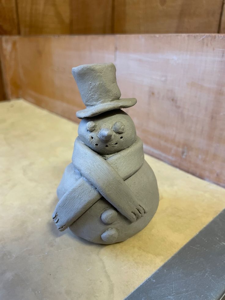 a clay sculpture of a bear holding a hat