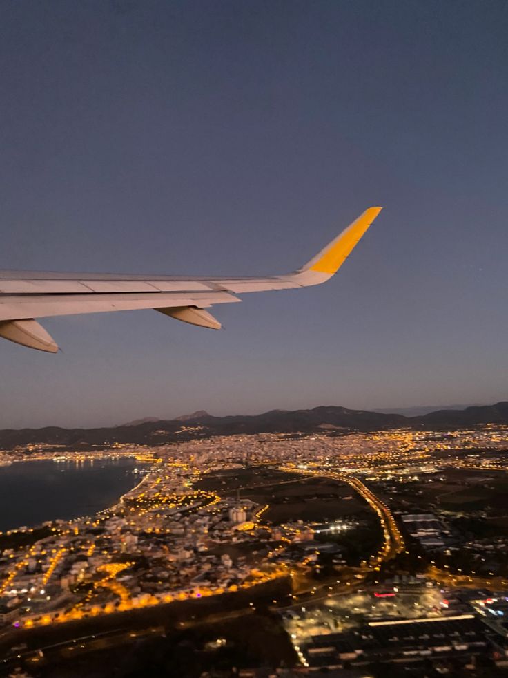 the wing of an airplane flying over a city at night with lights in the background