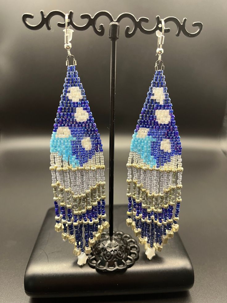 "Watch the clouds roll by over the mountains with this fun and sparkling earring. The bright blue sky and the deep blue waters are calming and full of life! Look at the little star on the fringe!  Silver-toned findings and glass seed beads - 5\" long" Blue Beaded Dangle Earrings For Beach, Adjustable Blue Bohemian Earrings, Blue Dangle Beaded Earrings For Beach, Blue Beaded Dangling Earrings For Festivals, Artisan Blue Beaded Earrings, Blue Beaded Earrings With Dangling Beads For Festival, Bohemian Blue Earrings With Dangling Beads, Blue Bohemian Earrings With Dangling Beads, Blue Beaded Fringe Jewelry For Beach