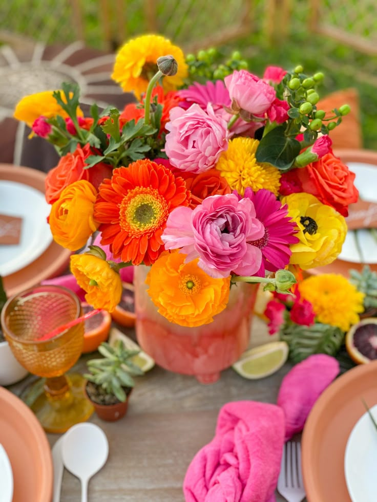 a vase filled with colorful flowers on top of a table next to plates and utensils