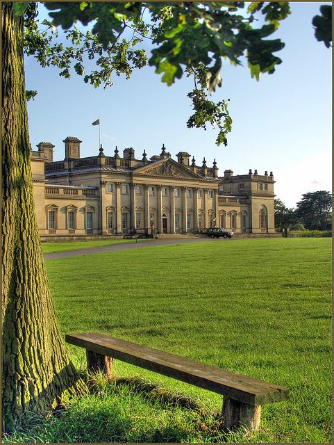 a bench sitting in front of a large building on top of a lush green field