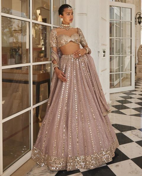 a woman in a pink and gold lehenga standing on a black and white checkered floor