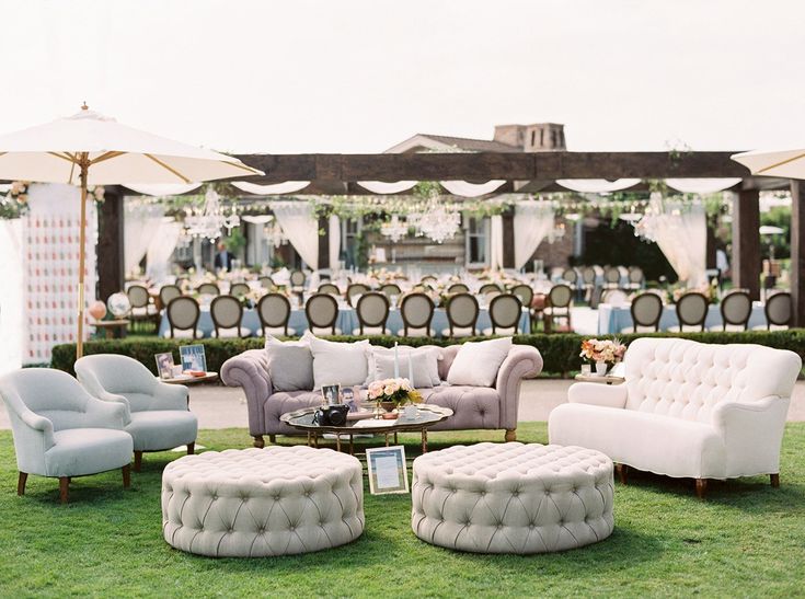 an outdoor seating area with couches, chairs and umbrellas on the grass at a wedding