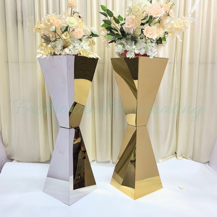 two gold and white vases with flowers in them on a tableclothed surface