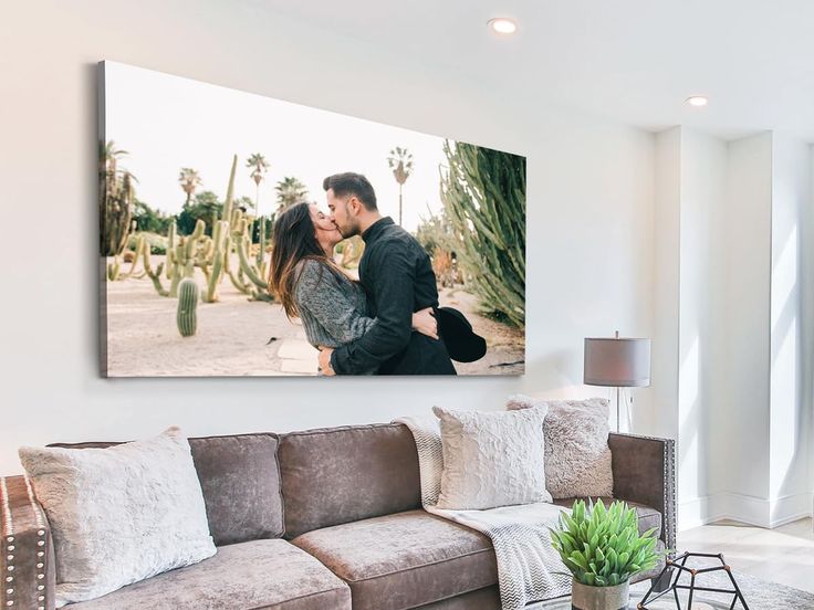 a man and woman kissing in front of a cactus print on a wall above a couch