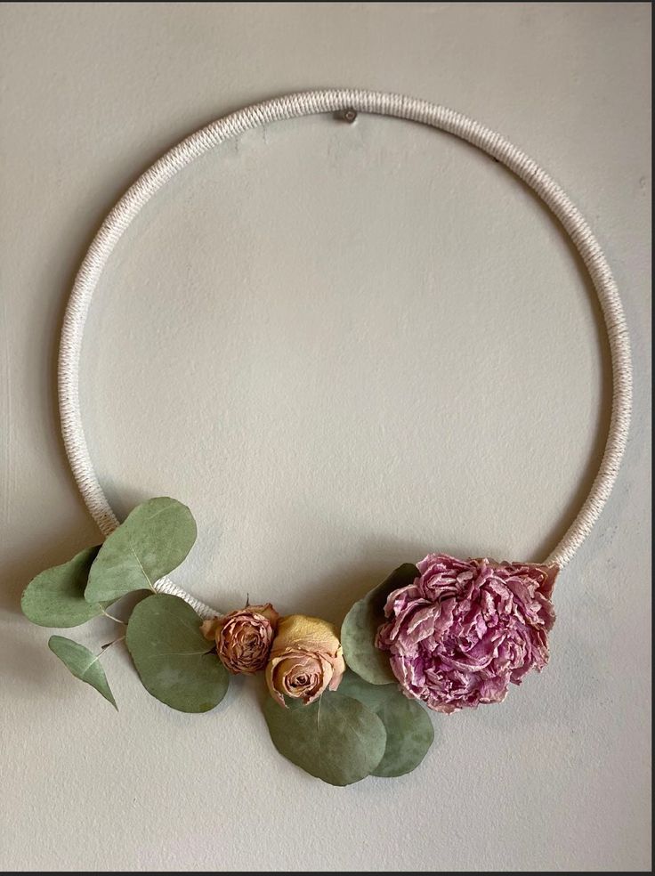 a white necklace with flowers and leaves on the front is hanging from a rope against a wall