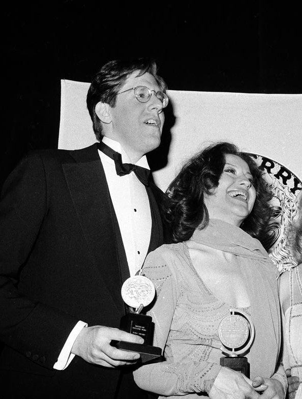 two people standing next to each other holding awards