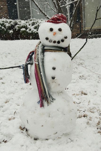 a snowman with a red hat and scarf standing in the snow