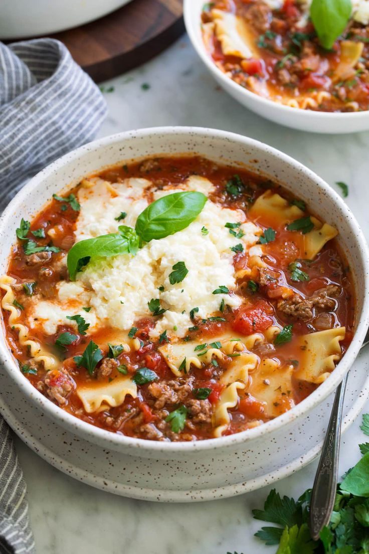 two bowls of pasta and meat soup with parmesan cheese on the top one