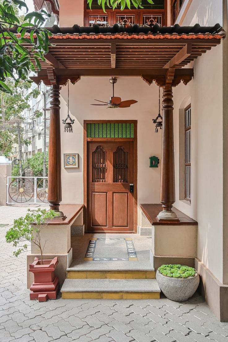 the front entrance to a house with wooden doors and pillars on both sides, surrounded by potted plants