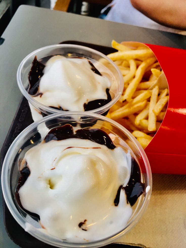 two plastic containers filled with ice cream and chocolate sauce next to french fries on a table