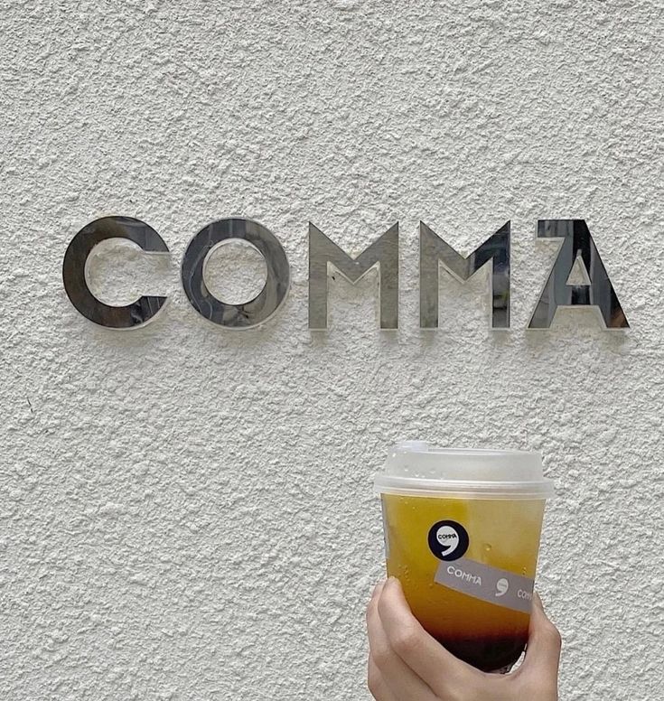 a person holding a cup in front of a sign that says comma