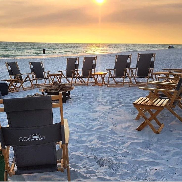 there are many chairs on the beach near the water and sun in the sky behind them