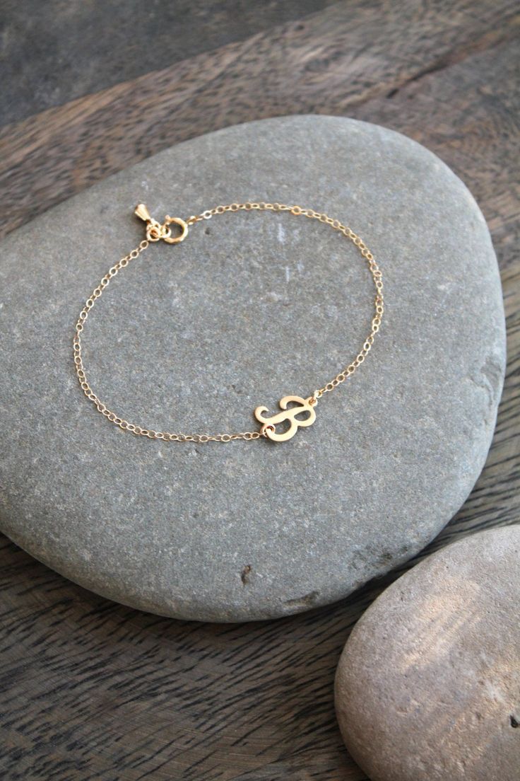 A dainty 14k gold filled bracelet with a script-letter initial, attached sideways on a shimmering chain, with a little teardrop charm by the clasp. Please select initial and size from the drop down menus. Available in the following letters only: A B C D E F H J K L M N P R S Y Components: Script letters - 14k gold filled, aprox 10x8mm each Chain - 14k gold filled Your item will arrive in a beautifully embossed Jewelry box - Ready for gift giving! Custom Name Adjustable 14k Gold Jewelry, Simple Custom Name Gold Jewelry, Simple 14k Gold Jewelry For Personalized Gifts, Dainty Adjustable Jewelry For Personalized Gift, Adjustable Dainty Jewelry For Personalized Gift, Simple Gold Jewelry With Custom Name, Dainty Adjustable Name Bracelet With Initials, Dainty Adjustable Initial Pendant Jewelry, Dainty Adjustable Bracelet With Initials