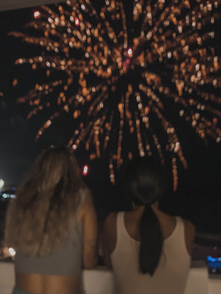 two women looking at fireworks in the night sky with their backs turned to the camera