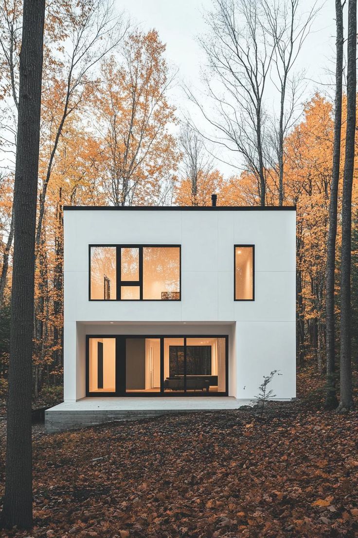 a white house in the woods surrounded by trees with lots of leaves on the ground